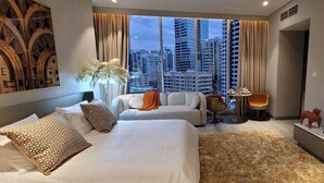 A hotel room with two beds, a TV, a small table with chairs, and a view of the cityscape.