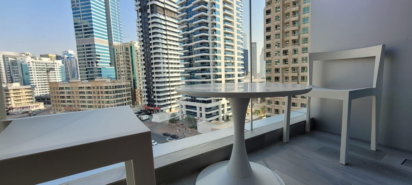 Een balkon met een ronde tafel en een stoel, met uitzicht op een stadsbeeld met moderne wolkenkrabbers.
