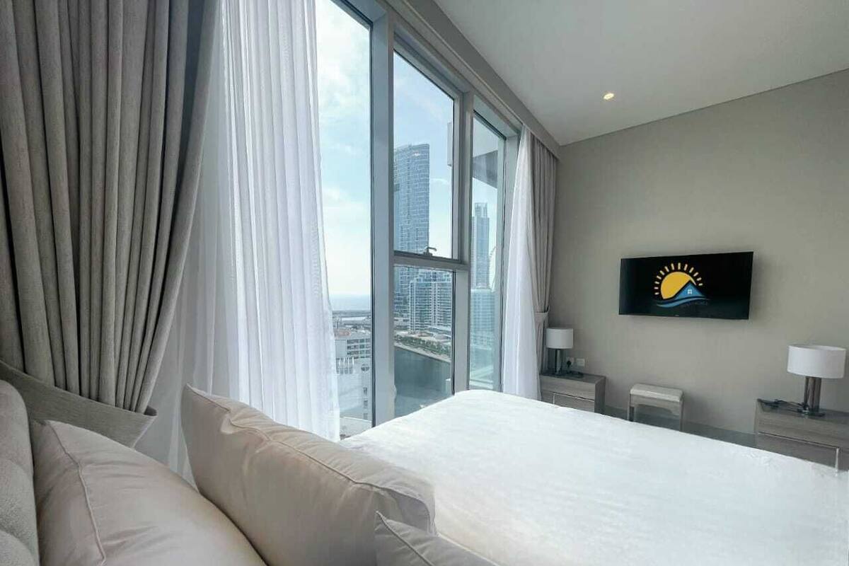 Een hotelkamer met een groot bed, een bank, een televisie aan de muur en uitzicht op de stad door grote ramen.