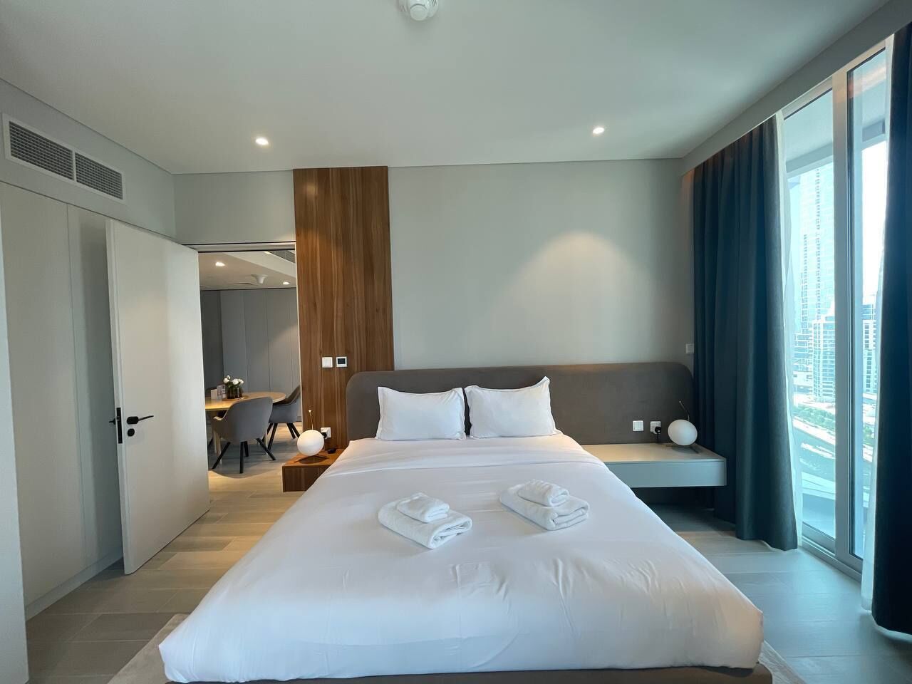 A modern hotel room with a large bed, a desk, and a view of the city.