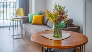 A modern living room with a round wooden table, a sofa with colorful cushions, and a vase with flowers. - HB apartments Marukhis (Tbilisi)