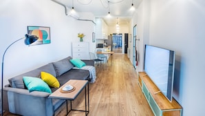 A modern living room with a sofa, coffee table, and TV. There is a kitchen in the background with a dining area. - HB apartments Marukhis (Tbilisi)