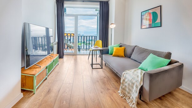 A modern living room with a grey sofa, wooden floor, and a TV on a wooden stand. - HB apartments Marukhis (Tbilisi)