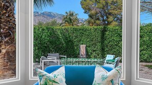 A room with a blue sofa, white furry rug, and a view of a garden with a table and chairs outside. - The Colony Hideaway - Pool Wifi Spa Private (Palm Springs)