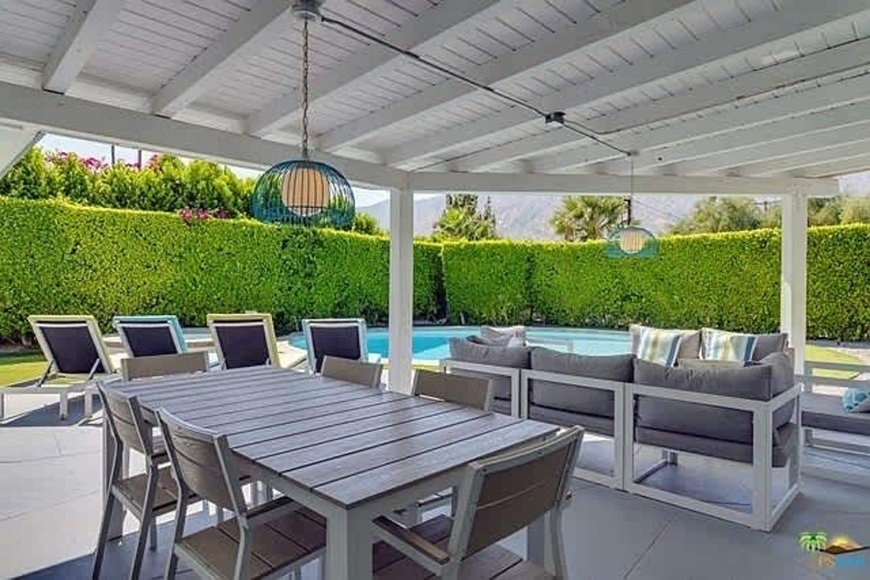 An outdoor patio with a pool, seating area, and a pergola with hanging lights.