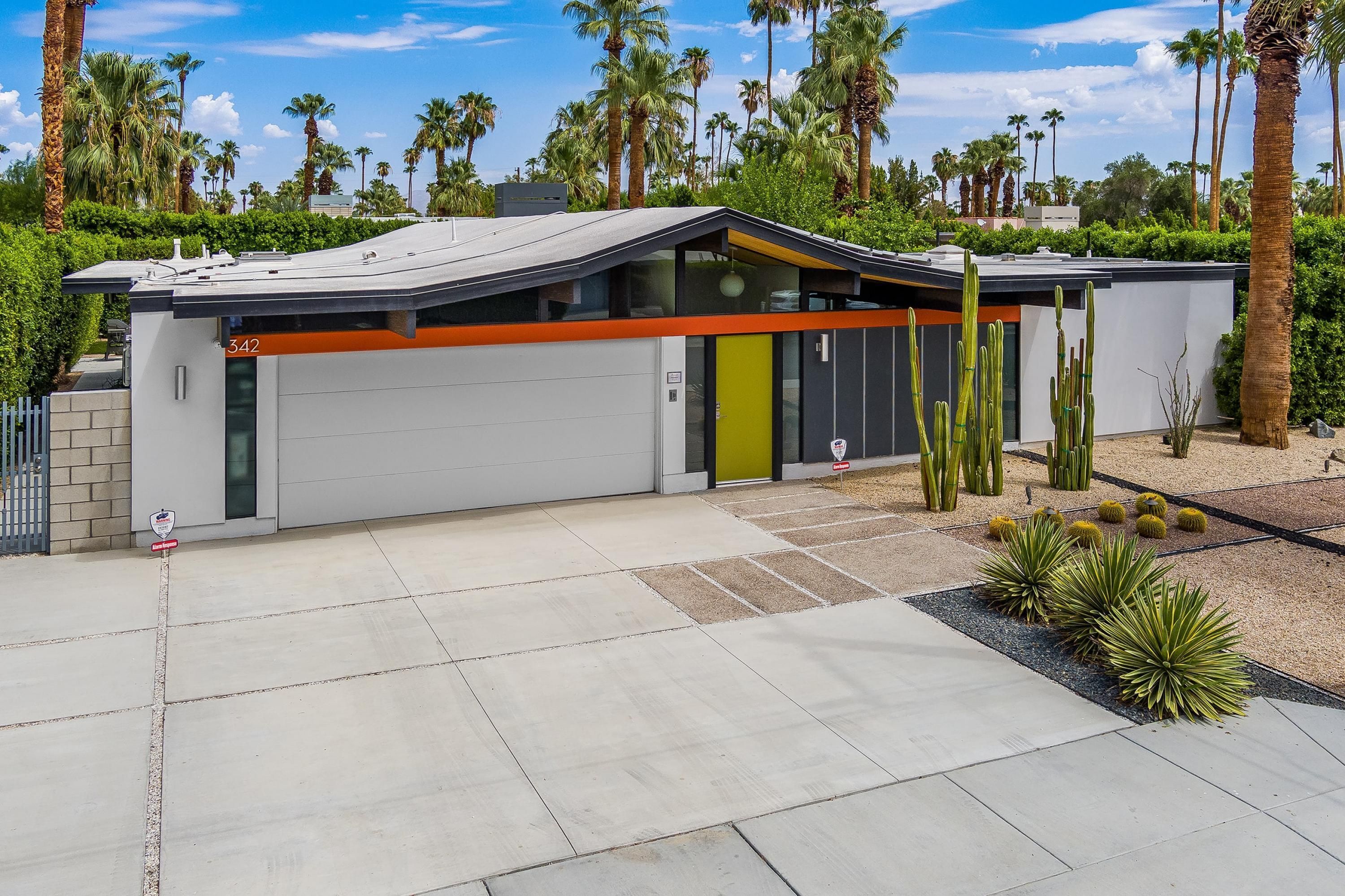 Een modern gebouw met een garagepoort, een nummer 342 bord en een kleine tuin met cactussen en vetplanten.