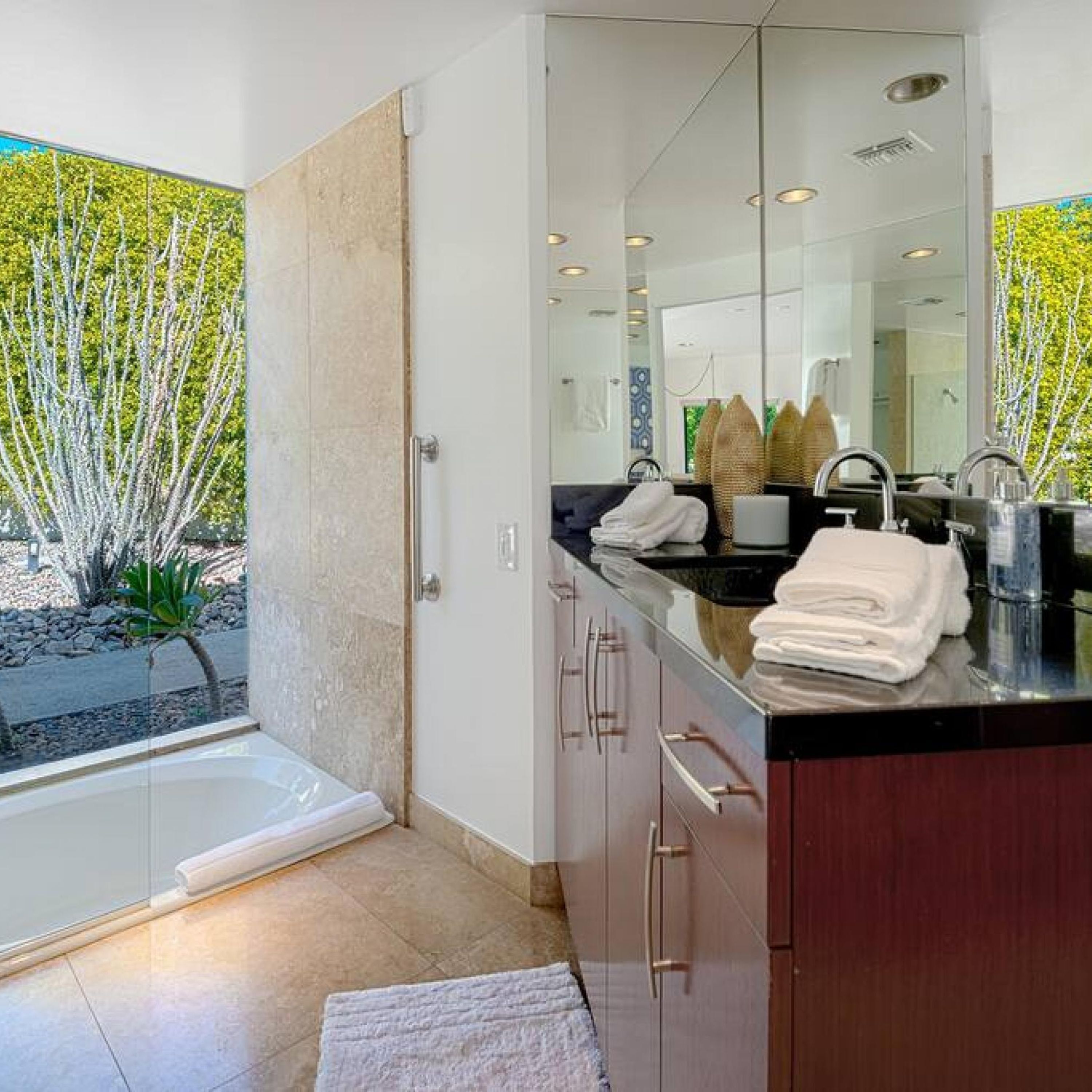 A modern bathroom with a large mirror, a bathtub, and a sink with towels.