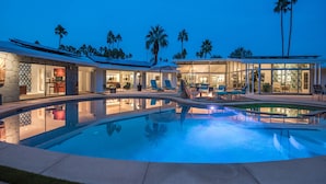 Una casa moderna con piscina, mobiliario exterior y palmeras.