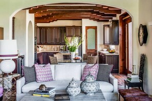 A cozy living area with a sofa, decorative vases, and books. A kitchen is visible in the background with wooden cabinets and a dining table. - Villa Vista in Palm Springs (Palm Springs)