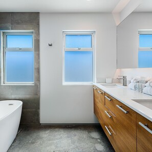 Un baño moderno con dos ventanas, una bañera y armarios de madera.