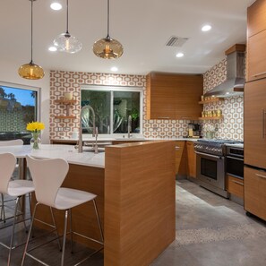 Una cocina moderna con una isla central, electrodomésticos de acero inoxidable e iluminación colgante.