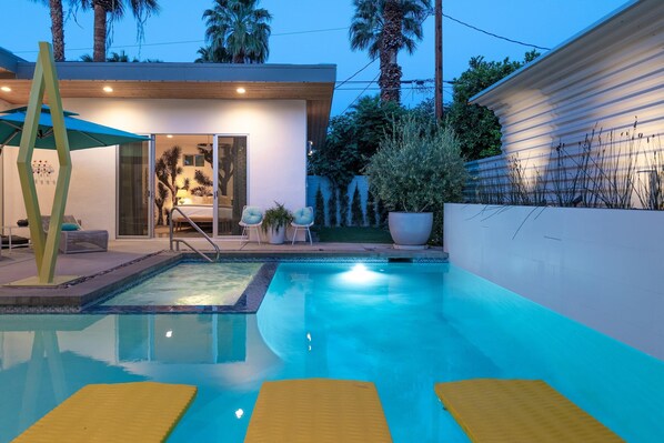 Zona de piscina moderna al aire libre, con vista despejada, colchonetas amarillas flotando y un patio con sillas y una mesa.