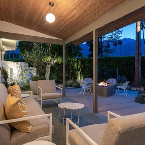 Un patio al aire libre con techo de madera, asientos acolchados y una chimenea.