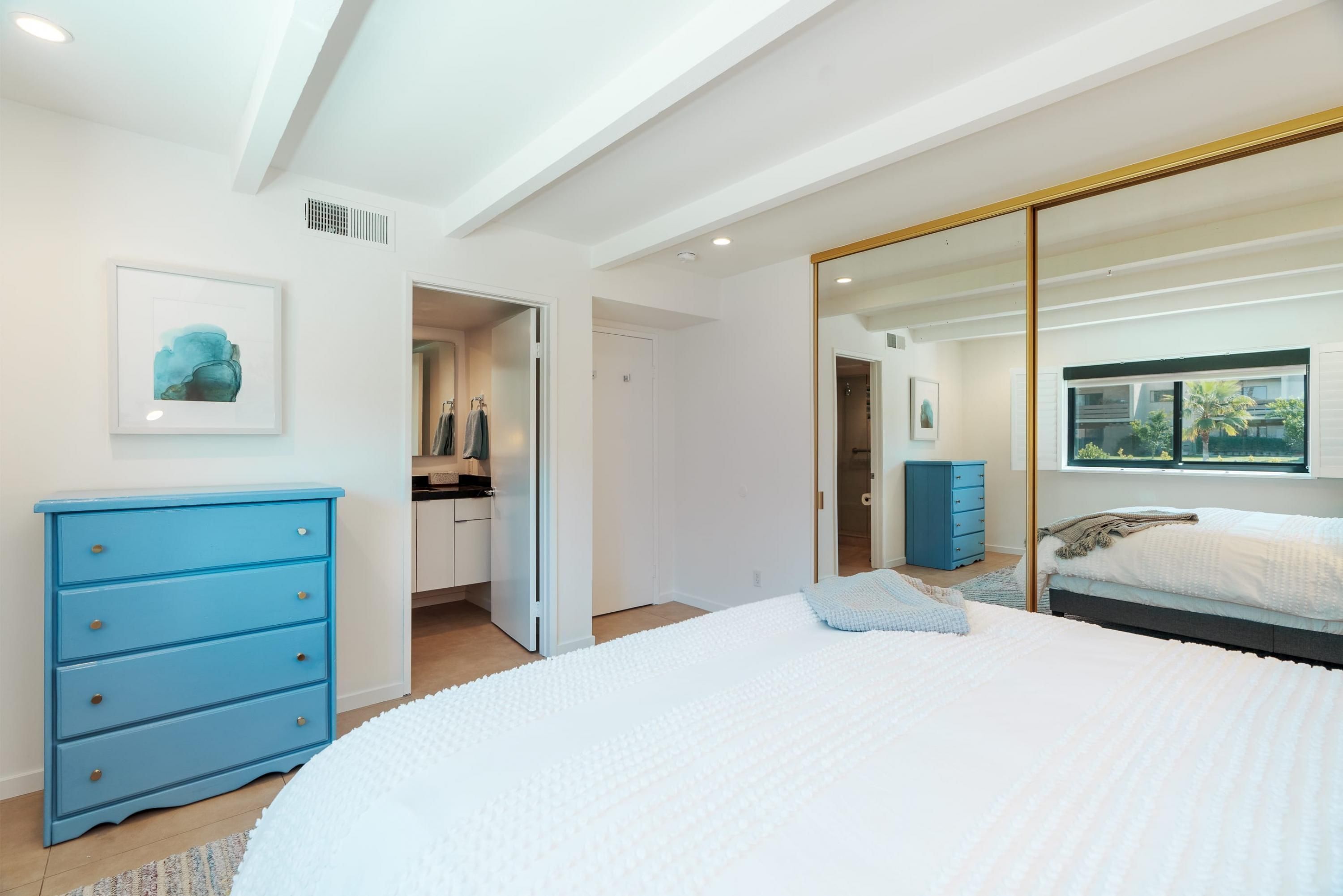 Une chambre à coucher moderne avec un grand lit, une commode bleue et un placard avec des portes miroir.