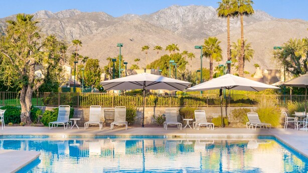 Un espace piscine agrémenté de chaises longues et de parasols, entouré de palmiers et avec des montagnes en toile de fond.