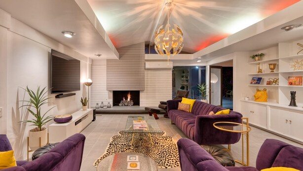 Ein modernes Wohnzimmer mit Kamin, violetten Sofas, einem Glastisch und einer außergewöhnlichen Deckenleuchte.