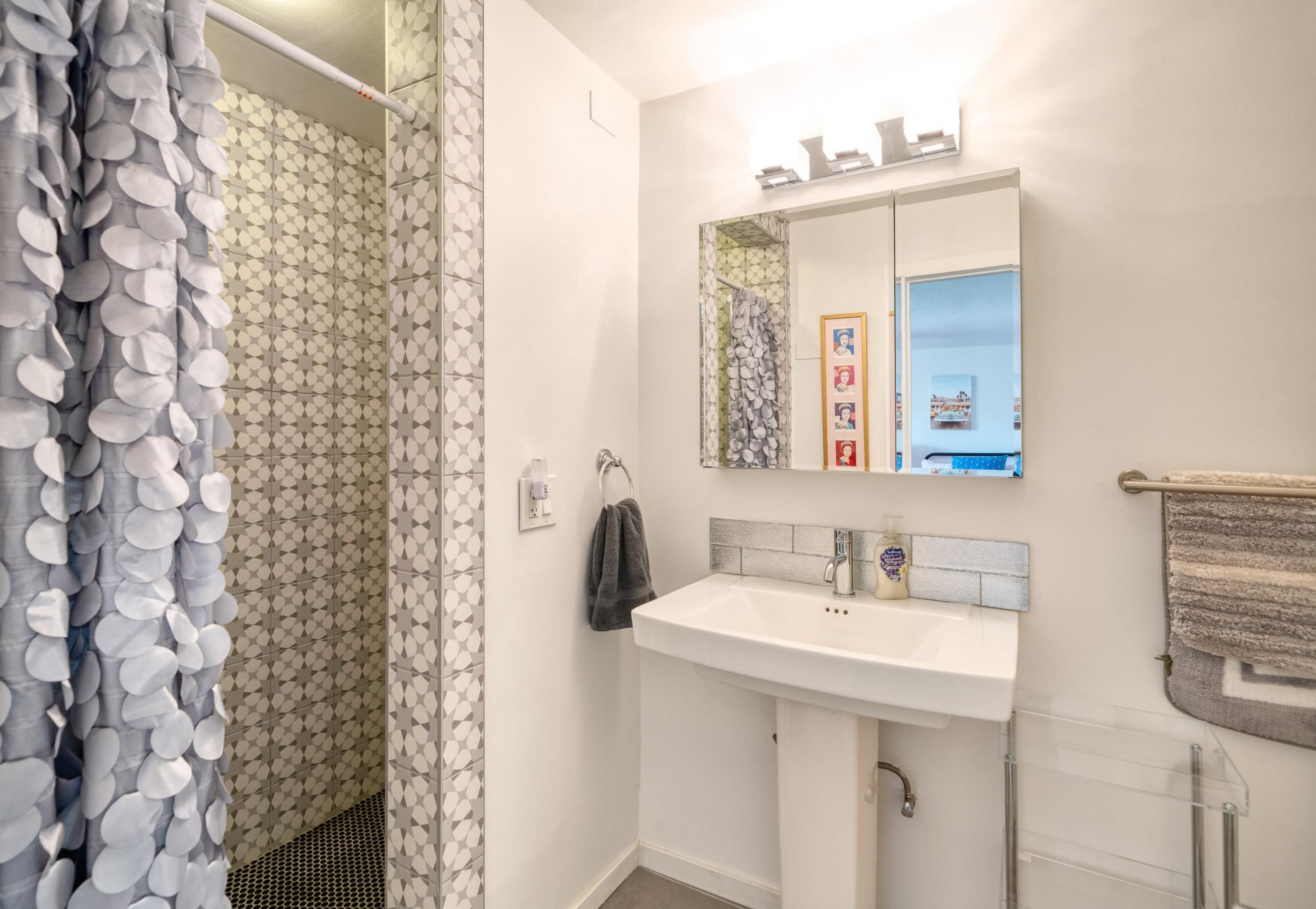 A bathroom with a white sink, mirror, and shower curtain with a geometric pattern.