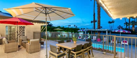 An outdoor patio with a pool, wicker furniture, and umbrellas.