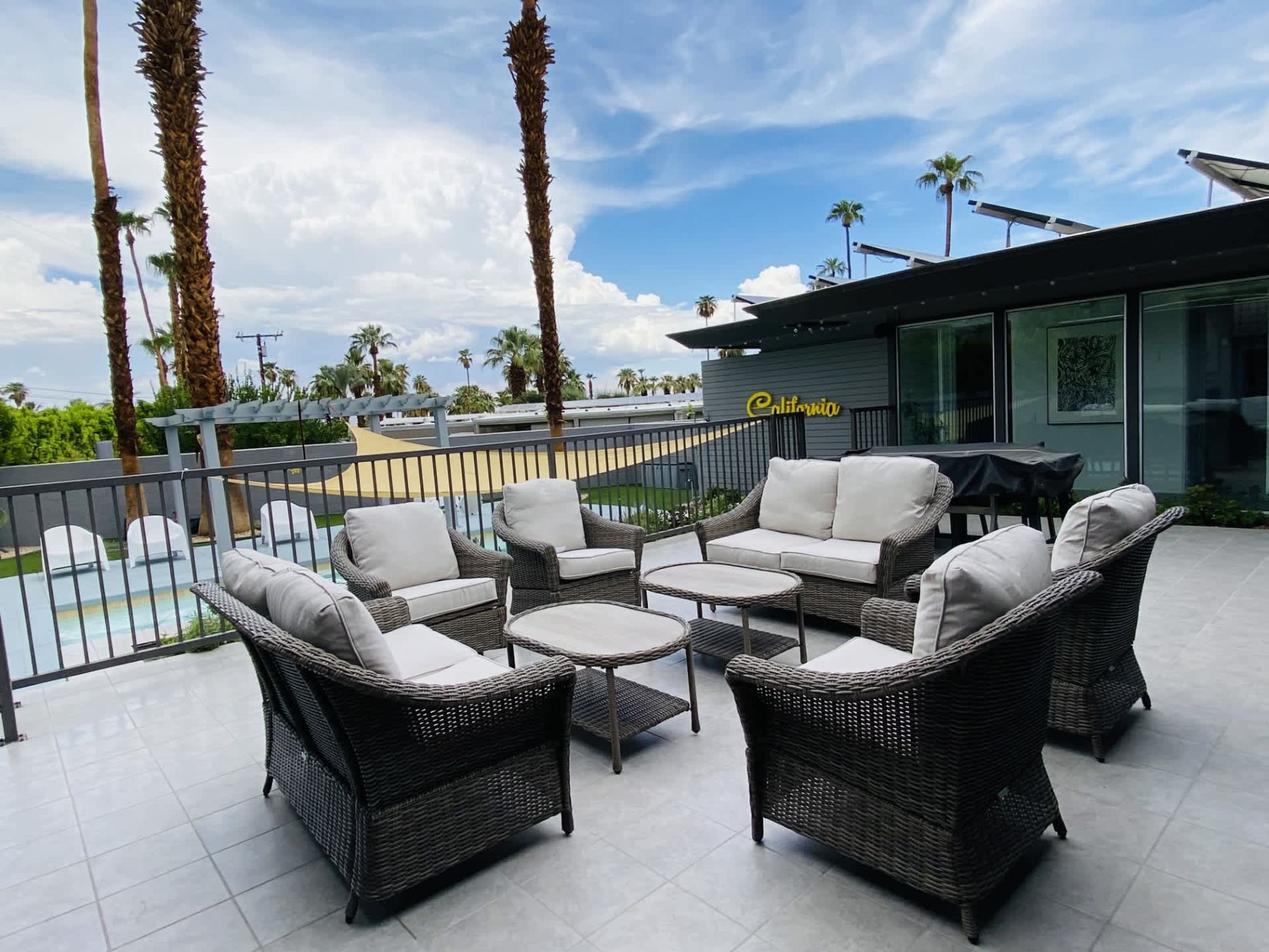 A patio with wicker furniture, a pool, and palm trees.