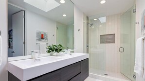 Une salle de bain moderne avec un grand miroir, un meuble-lavabo blanc, une douche en verre et une plante en pot.
