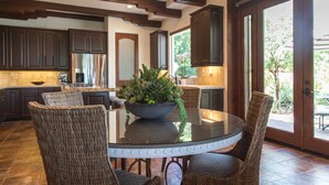 A kitchen with dark wooden cabinets, a glass-top dining table, wicker chairs, and a potted plant. - Villa Vista - Spanish Luxury Pool Wifi (Palm Springs)