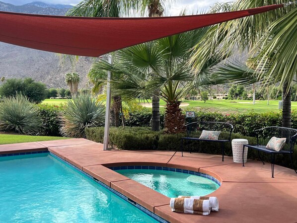 Une piscine à bord incurvé, entourée d’un patio aménagé avec des meubles d’extérieur, des palmiers, et offrant une vue sur un terrain de golf et des montagnes en arrière-plan.