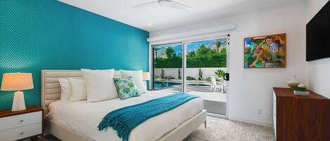 A modern bedroom with a large bed, a ceiling fan, a view of a swimming pool, and a painting on the wall.