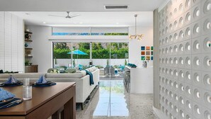Eine moderne Küche mit großem Fenster, einem Essbereich mit Tisch für Zwei und einer Wohnbereich mit Sofa und Sesseln.