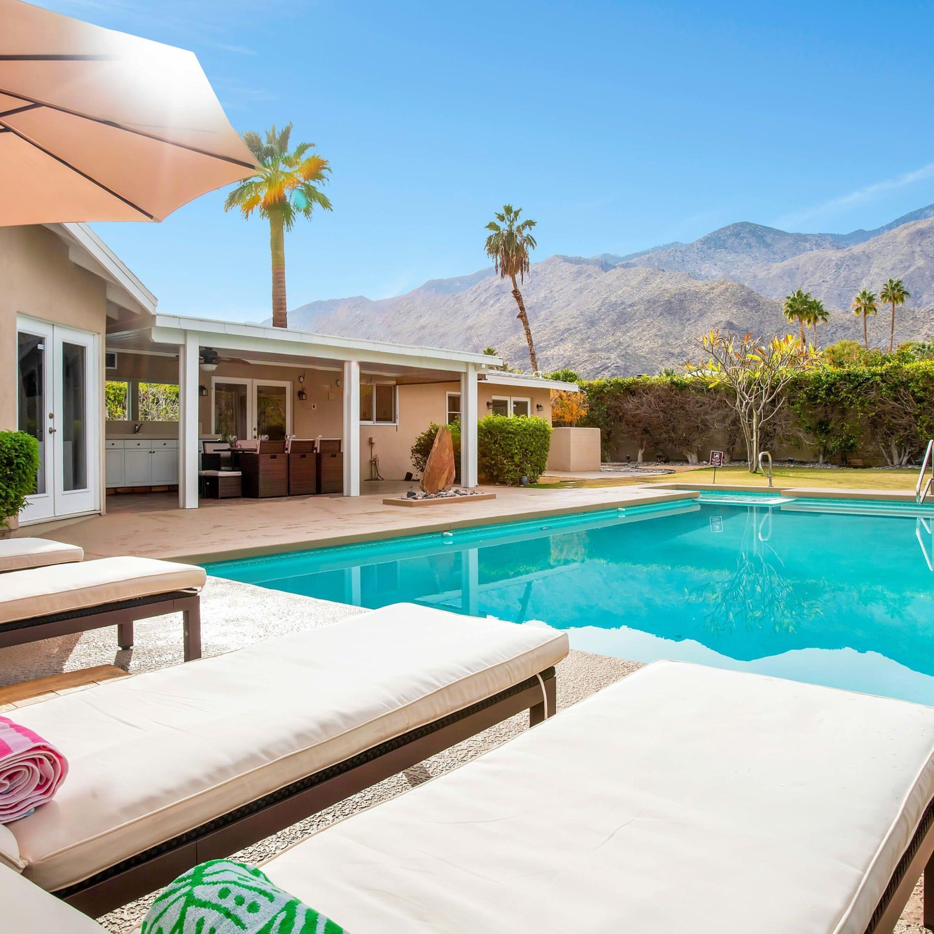 A poolside area with lounge chairs, a covered patio, and a mountain backdrop.