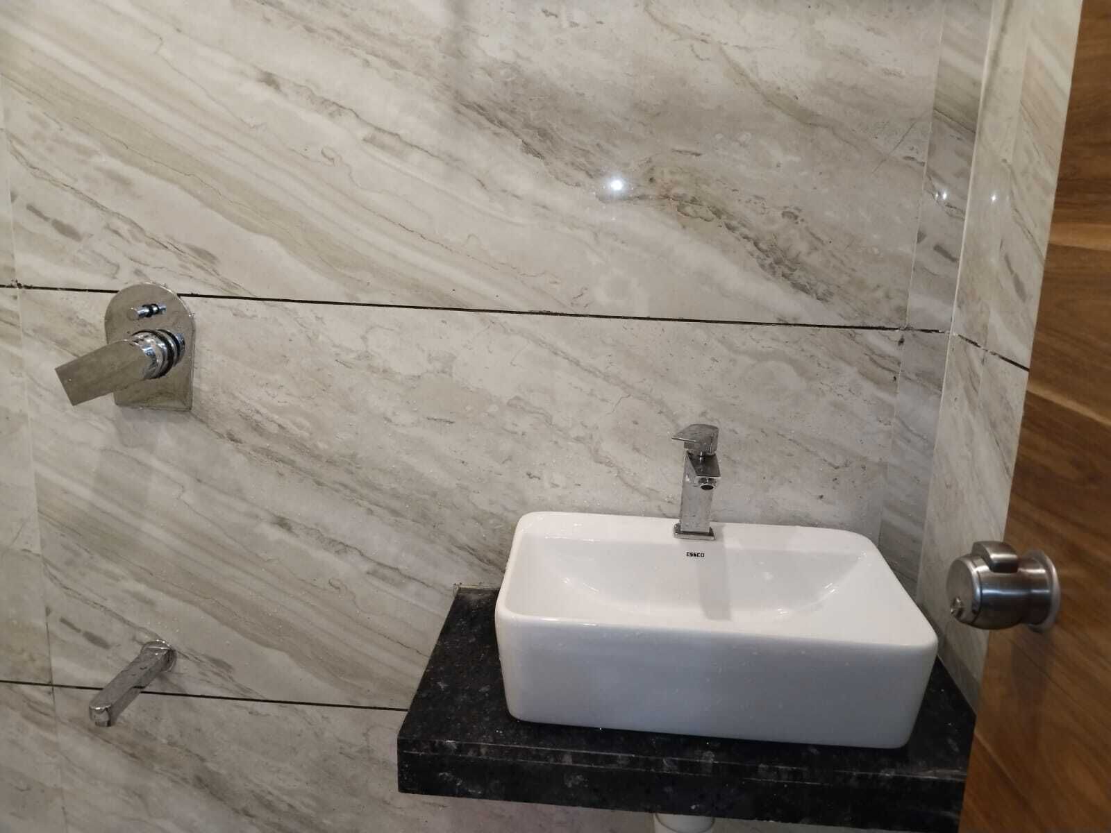 A bathroom with a white sink on a black countertop, a silver faucet, and a door with a silver handle.