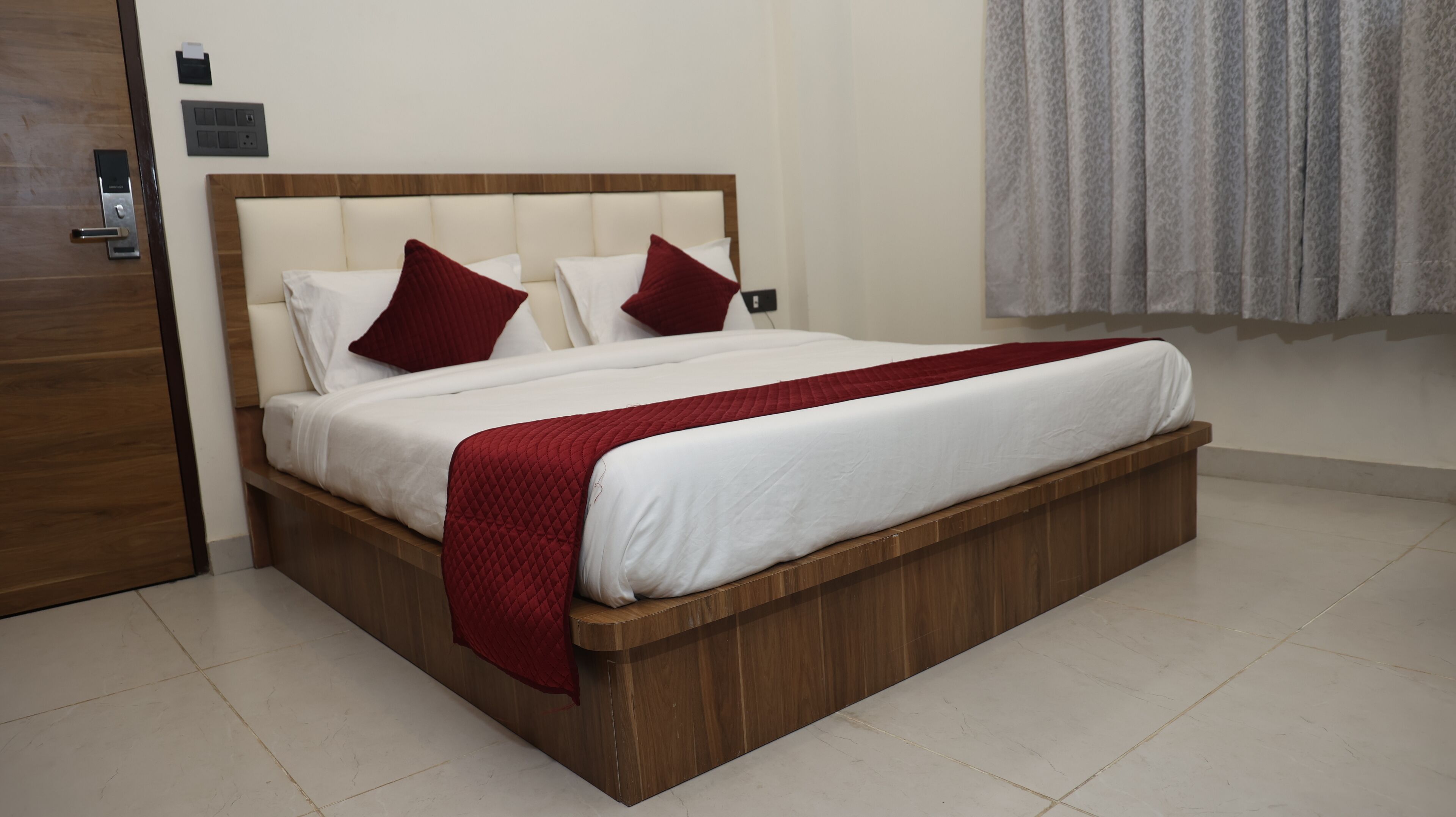 Quarto de hotel moderno com estrutura de cama de madeira, roupa de cama branca e almofadas decorativas vermelhas.