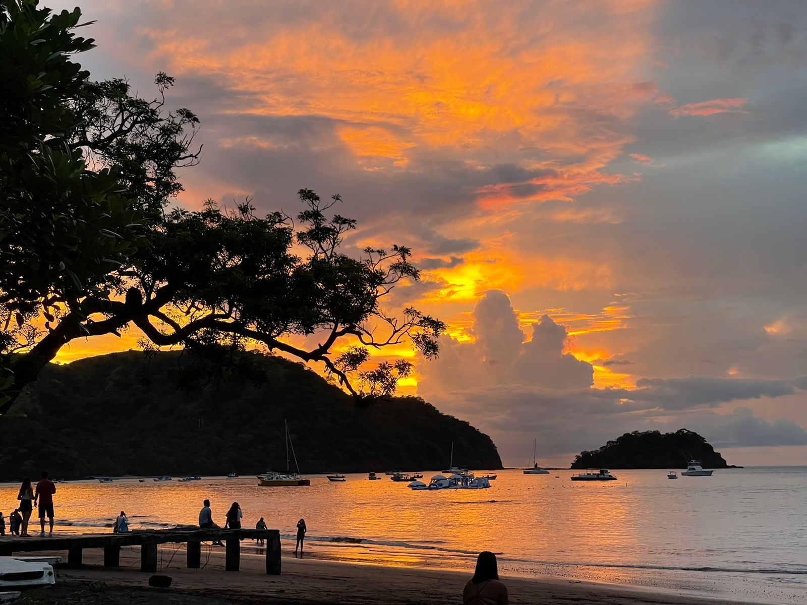 Escena de playa con barcos y gente durante el atardecer.