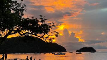 Escena de playa con barcos y gente durante el atardecer.