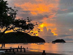 Escena de playa con barcos y gente durante el atardecer.