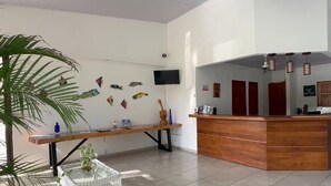 A reception area with a wooden reception desk, a bench, and a wall-mounted TV. - The Palms At Coco Beach (Carrillos)