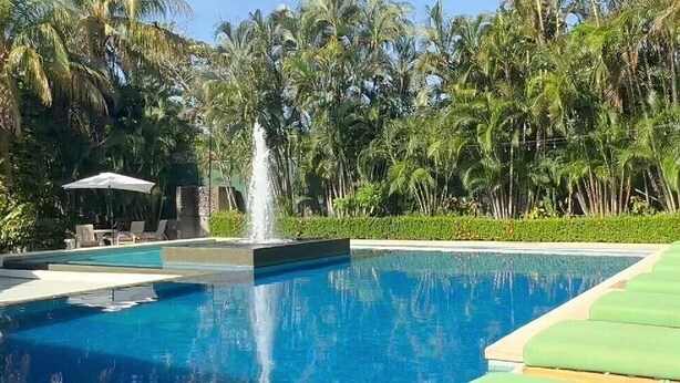 A swimming pool with a fountain, surrounded by lush greenery and a row of green lounge chairs. - The Palms At Coco Beach (Carrillos)