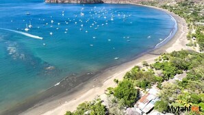 An aerial view of a coastal area with a beach, boats, and a mountainous backdrop. - The Palms At Coco Beach (Carrillos)