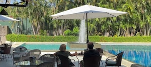 Zona junto a la piscina con una cascada, mobiliario exterior y abundante vegetación de fondo.