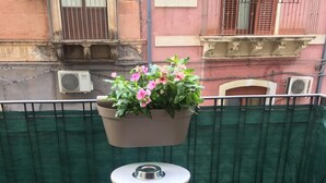 Ein kleiner Sitzbereich im Freien mit zwei Hocker, einem Tisch und einem hängenden Blumentopf mit Blumen.