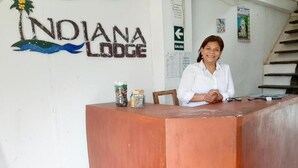 A reception desk at Indiana Lodge with a wooden counter, a woman seated behind it, and a wall with a logo and directional sign. - Indiana Lodge (Indiana)