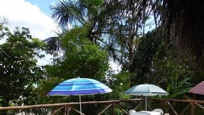 An outdoor wooden deck with white plastic chairs and tables, surrounded by lush greenery and a thatched roof structure. - Indiana Lodge (Indiana)