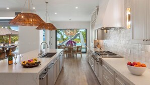 Een moderne keuken met een centraal eiland, roestvrijstalen apparatuur en uitzicht op een zwembad en glijbaan.