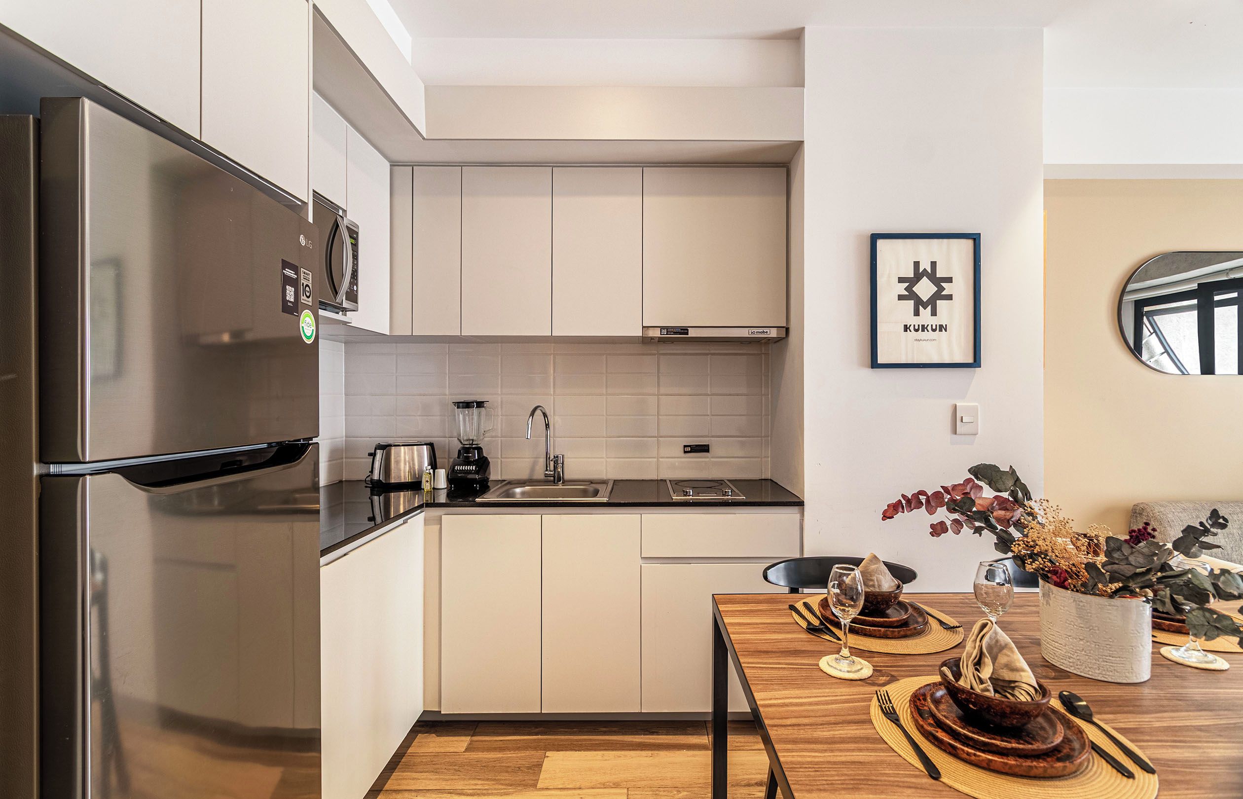 Cocina moderna con electrodomésticos de acero inoxidable, encimera negra y comedor con mesa de madera para dos.