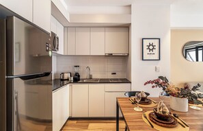 Cocina moderna con electrodomésticos de acero inoxidable, encimera negra y comedor con mesa de madera para dos.