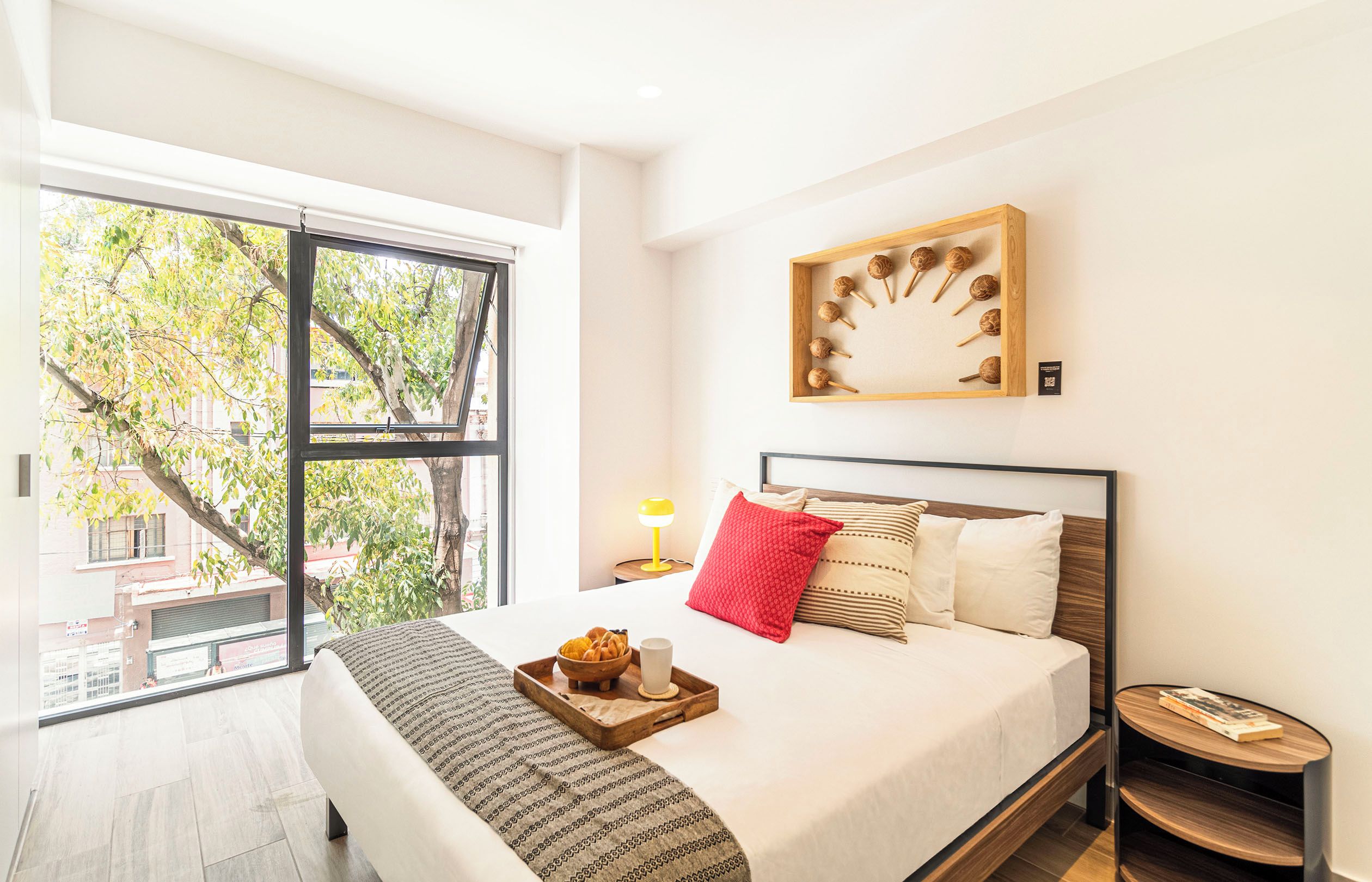 Un dormitorio moderno con un ventanal grande, una cama con cabecera de madera, una mesita de noche con lámpara y una obra de arte colgada en la pared.