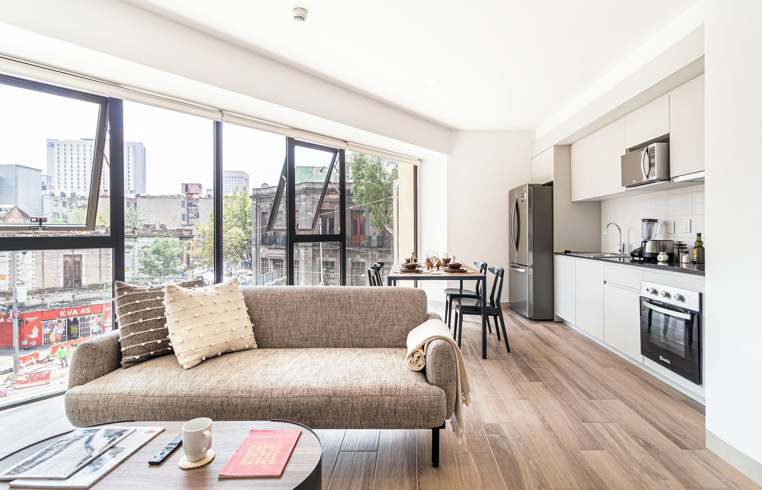 Un apartamento moderno con un ventanal grande, un sofá, una mesa de comedor y una zona de cocina.