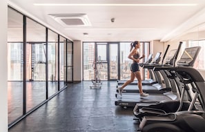 A gym with treadmills, a rowing machine, and large windows offering a city view. - Kukun Reforma Downtown (Mexico City)