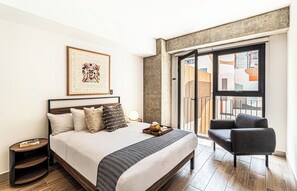 A modern bedroom with a large bed, a side table, a chair, a framed artwork, and a balcony with a view. - Kukun Reforma Downtown (Mexico City)