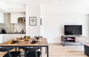 A modern kitchen with a microwave, dining table set with plates, bowls, and glasses, and a flat-screen TV on a stand. - Kukun Reforma Downtown (Mexico City)