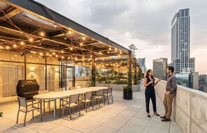Une terrasse extérieure avec une table et des chaises, des guirlandes lumineuses et un barbecue.